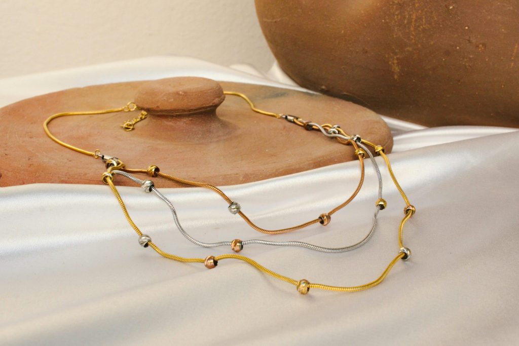 Stylish necklaces displayed elegantly on a white fabric with a rustic clay pot backdrop.